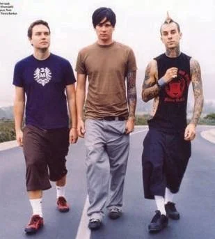 Blink-182 walking down a road, with Travis Barker in Dickies work shorts and pulled-up white socks