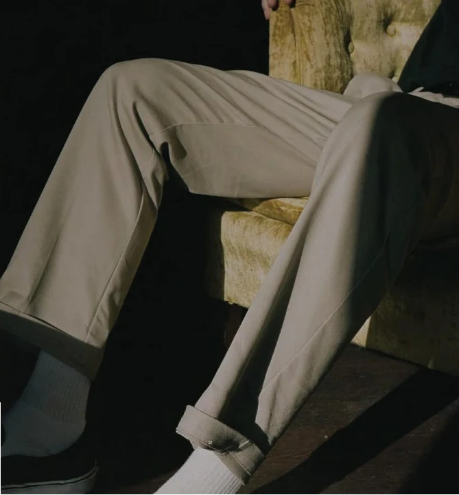Close-up of khaki work trousers with rolled cuffs and white socks on a person seated in a gold velvet armchair