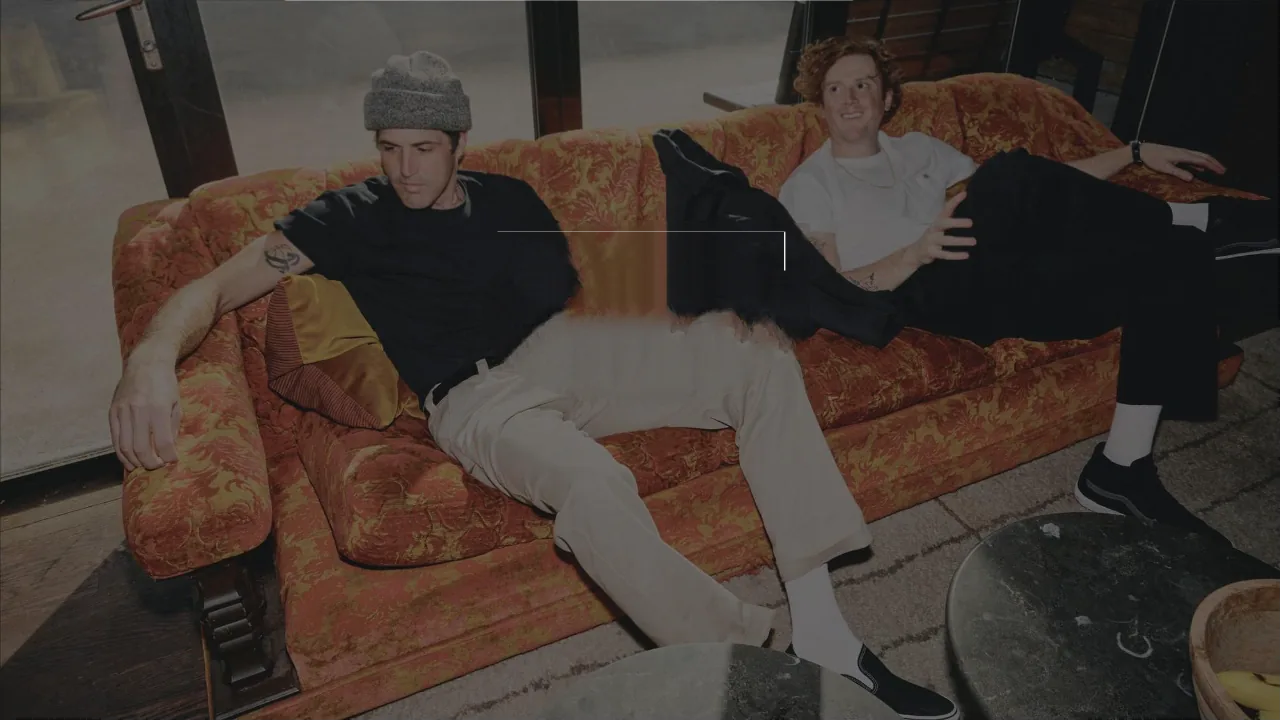 Two friends relaxing on a vintage orange sofa in Dickies workwear trousers and tees