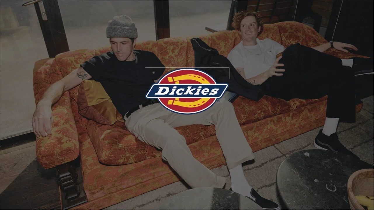 Two friends relaxing on a vintage orange sofa in Dickies workwear, with the Dickies logo in the centre