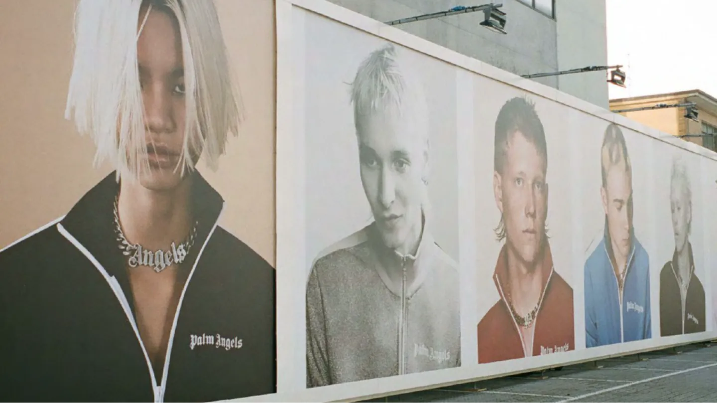 Palm Angels billboard campaign along a street wall showing portraits of young models in track jackets